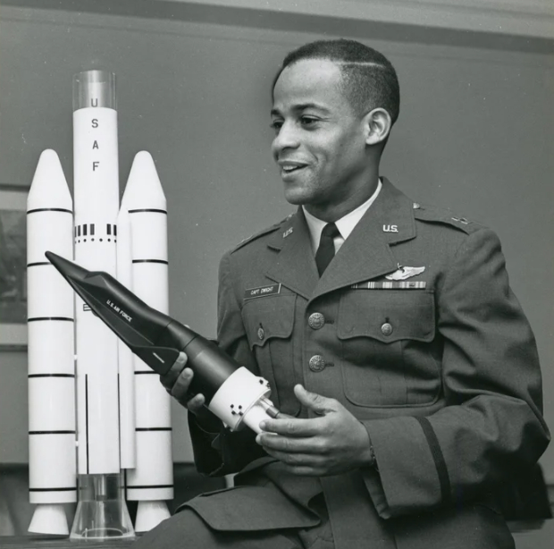 Dwight jeune en tenue militaire dans un bureau, tenant une maquette de navette spatiale, maquette de fusée en arrière-plan.