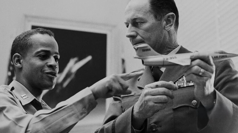 Dwight jeune et Chuck Yeager discutant dans un bureau d'une maquette d'avion que tient Yeager.