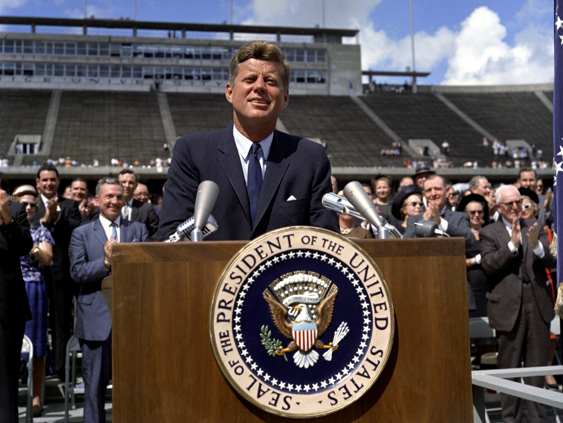 Kennedy devant un pupitre, une foule l'applaudit en arrière-plan.